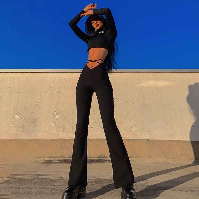 Fashion model wearing stylish black flared track pants with high comfort and a cropped top against a blue sky