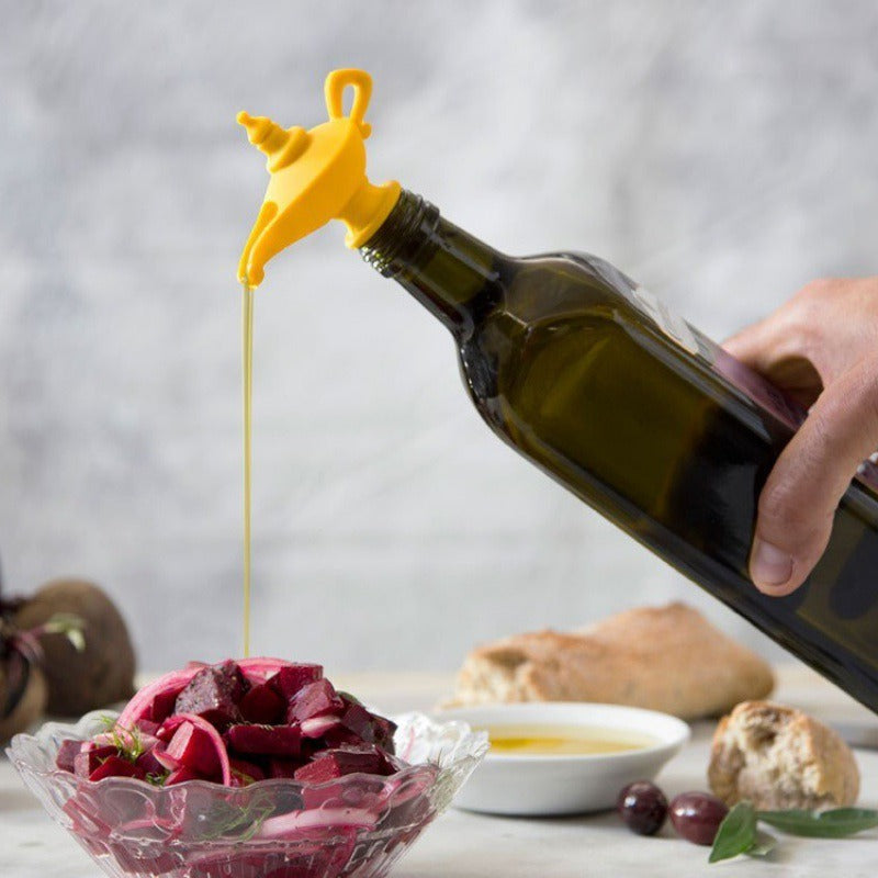 Silicone Aladdin lamp wine pourer pouring oil into a glass bowl with salad on a table